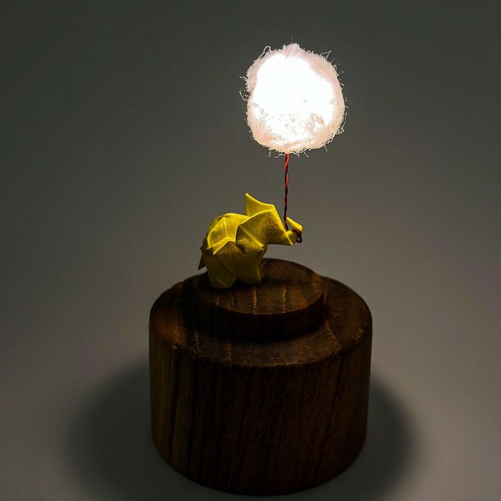 Lámpara miniatura de elefante amarillo en origami sosteniendo una nube iluminada en domo de vidrio - Plicatorius.