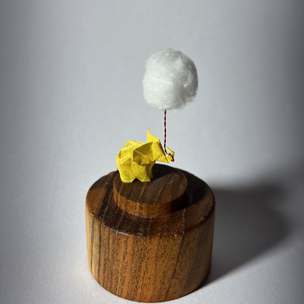 Lámpara miniatura de elefante amarillo en origami sosteniendo una nube iluminada en domo de vidrio - Plicatorius.