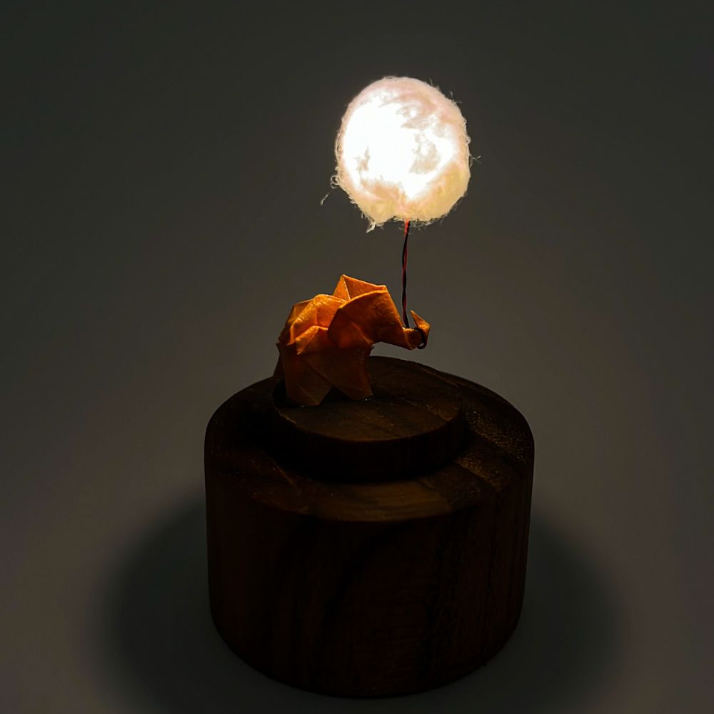 Lámpara miniatura de elefante amarillo en origami sosteniendo una nube iluminada en domo de vidrio - Plicatorius.