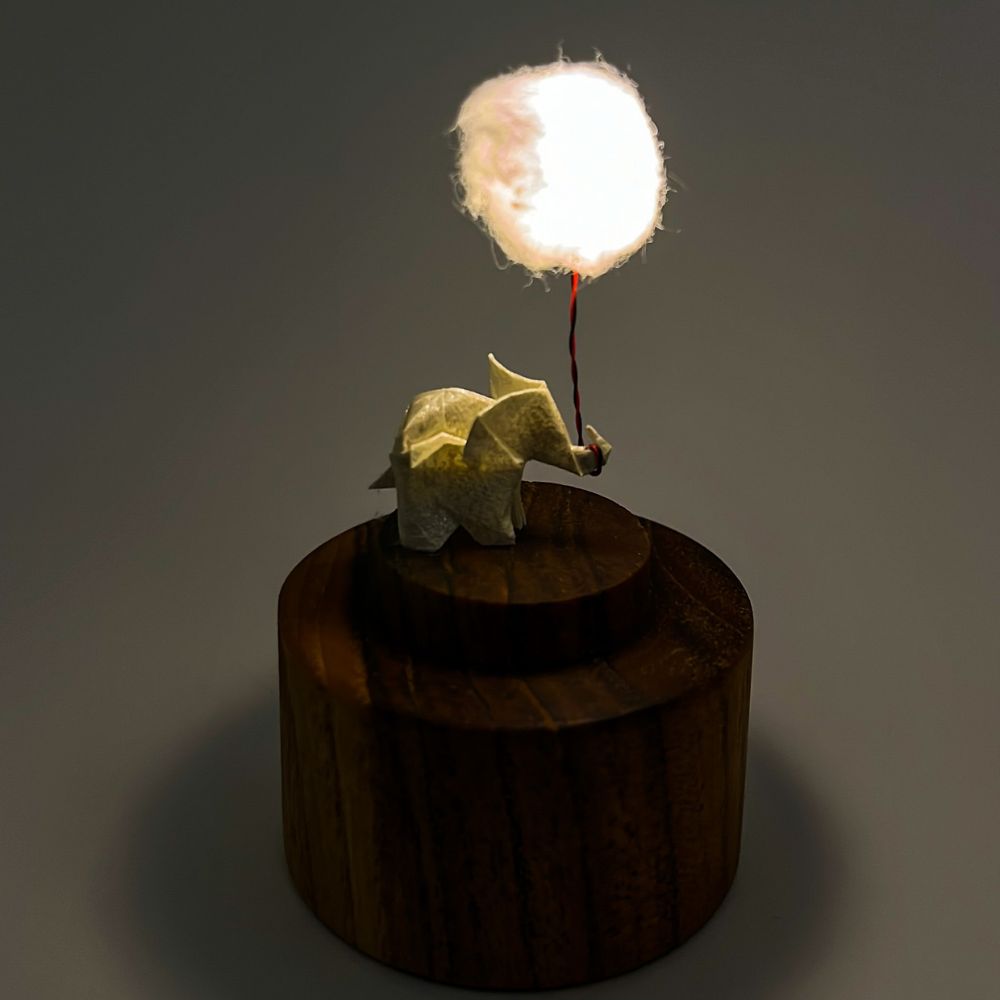 Lámpara miniatura de elefante amarillo en origami sosteniendo una nube iluminada en domo de vidrio - Plicatorius.