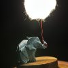 Lámpara miniatura de elefante amarillo en origami sosteniendo una nube iluminada en domo de vidrio - Plicatorius.